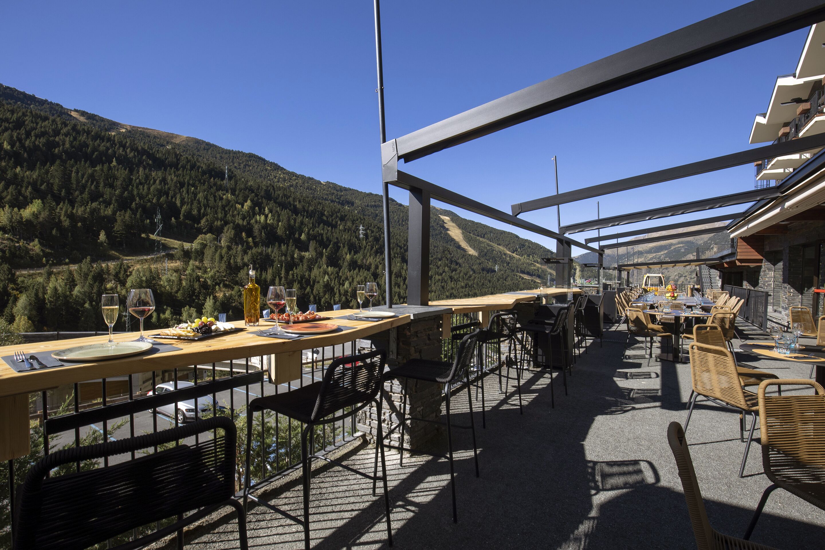 An outdoor dining area with tables and chairs, overlooking a mountainous landscape.