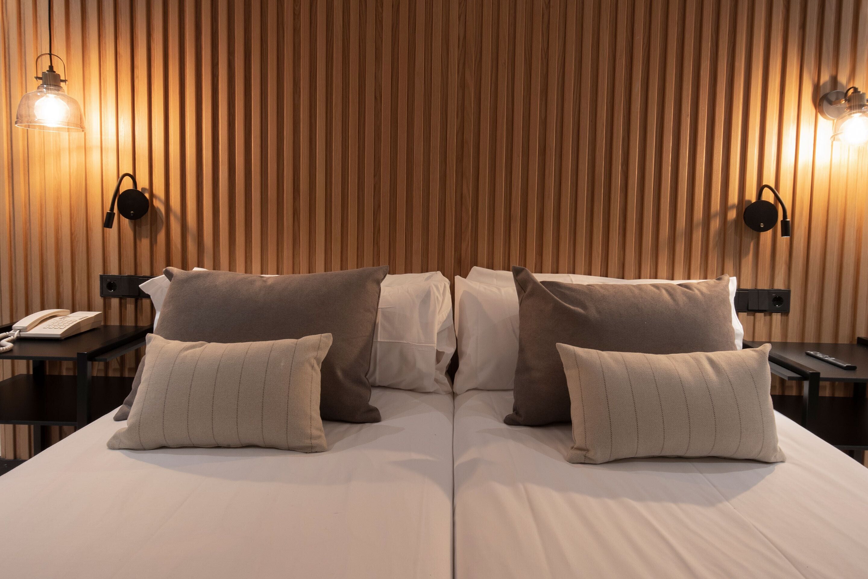 A hotel room with a wooden slat wall, two bedside tables with lamps, and a bed with multiple pillows.