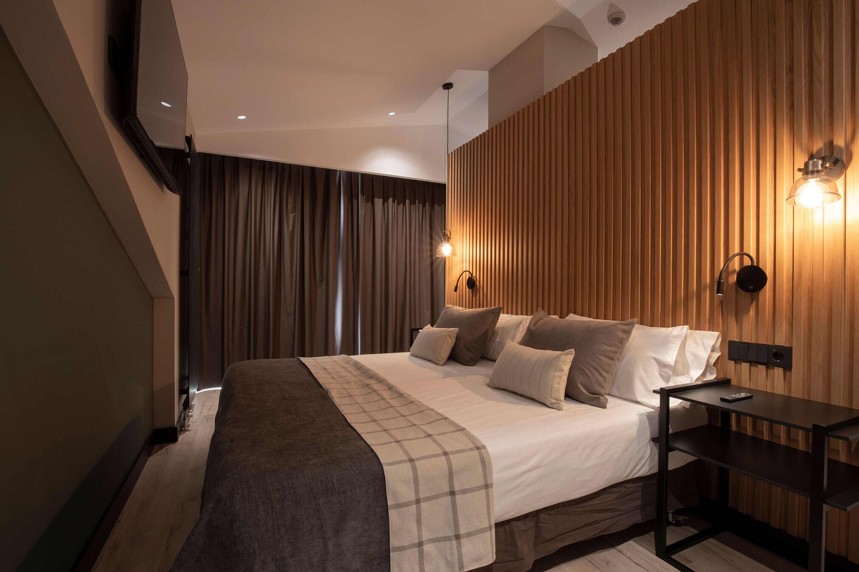 Una habitación de hotel moderna con una cama grande, un panel de pared de madera y una mesita de noche con lámpara.