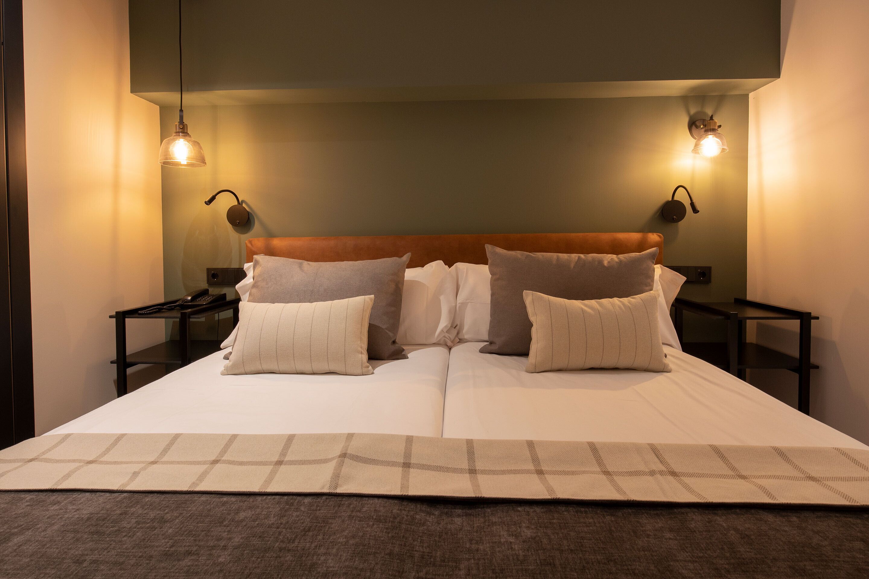 A neatly made bed with a headboard, two bedside tables, and two wall-mounted lamps.