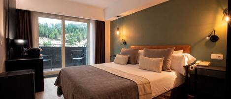 Quarto de hotel com uma cama grande, uma escrivaninha, uma cadeira, uma televisão e vista para uma floresta pela janela.