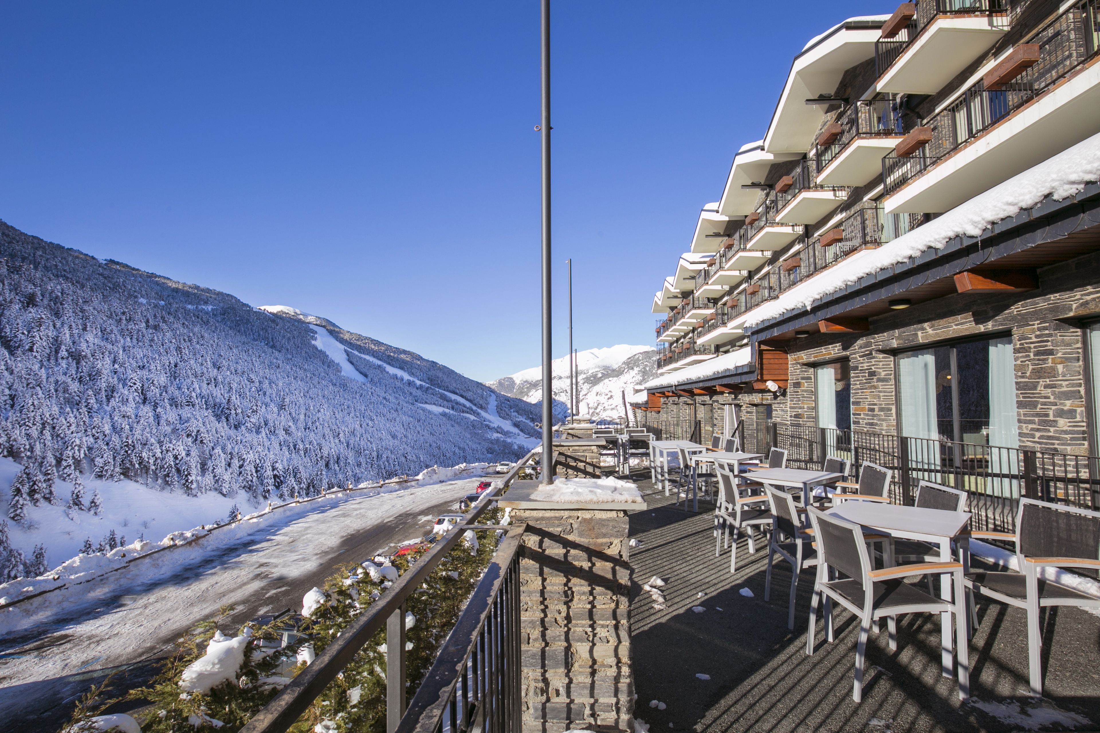 A hotel with outdoor seating overlooking a snowy mountain and a river.