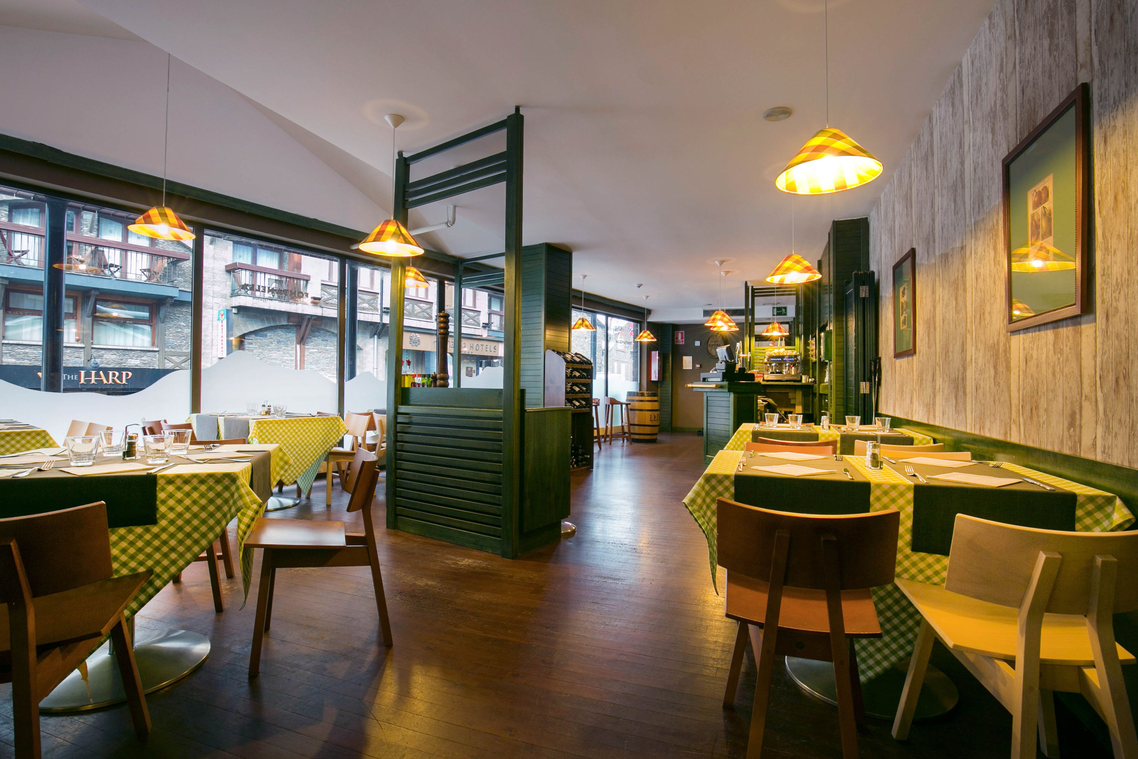 A restaurant with multiple tables and chairs, wooden floors, and hanging pendant lights.