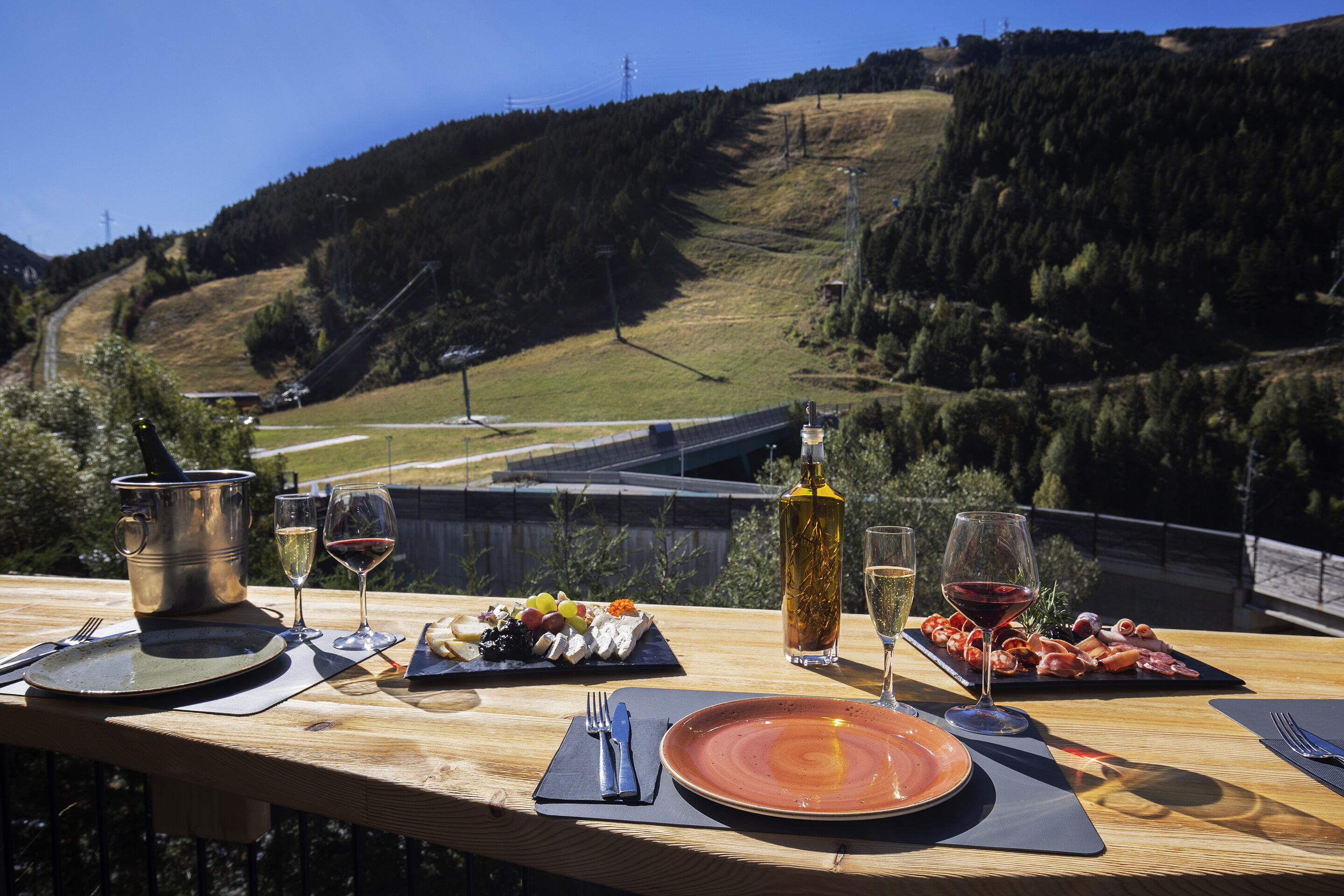 Ein Holztisch, gedeckt mit verschiedenen Speisen und Getränken, mit Blick auf eine malerische Berglandschaft.