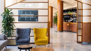 Un hall con dos sillones, un sofá, una mesa redonda de madera y una zona de bar con estanterías llenas de botellas.