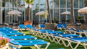 Zona de piscina con tumbonas, sombrillas y palmeras.