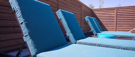 A row of outdoor lounge chairs with blue cushions against a wooden wall.