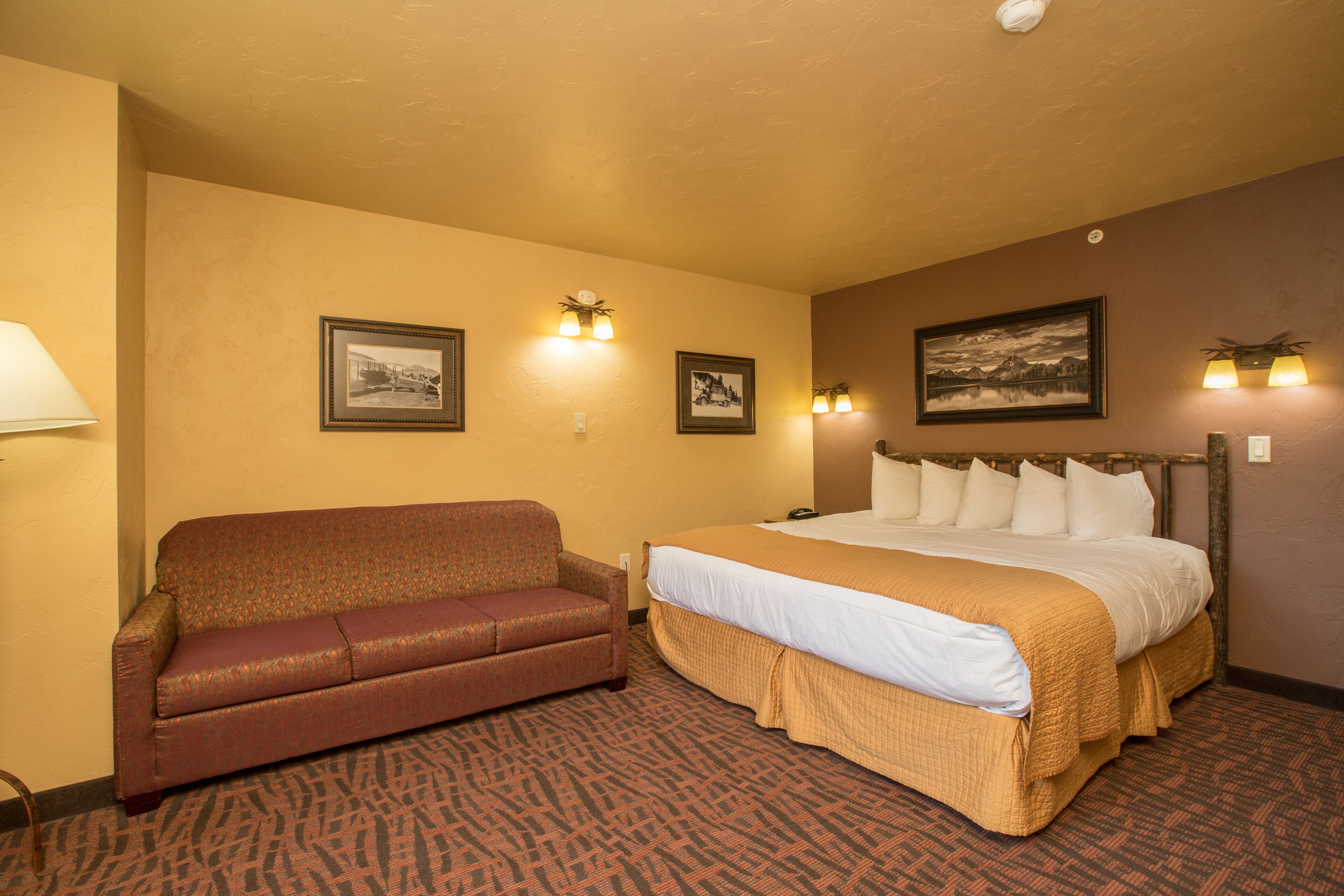 A hotel room with a bed, a sofa, and two wall-mounted lamps.