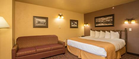 A hotel room with a bed, a sofa, and two wall-mounted lamps.