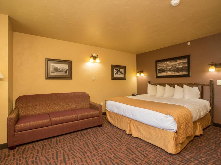 A hotel room with a bed, a sofa, and two wall-mounted lamps.