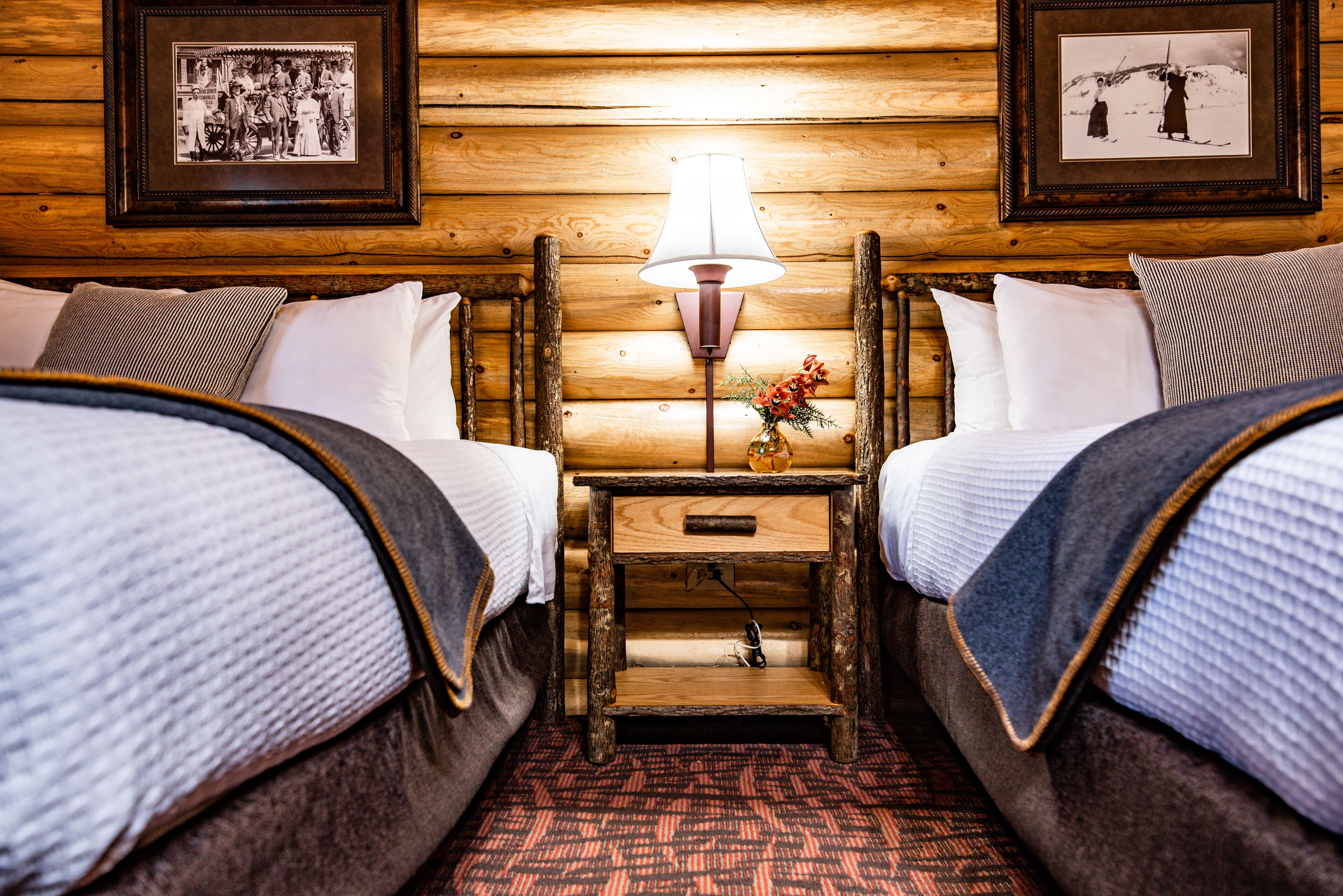 Una habitación acogedora con dos camas, una mesita de noche con lámpara y cuadros en las paredes.