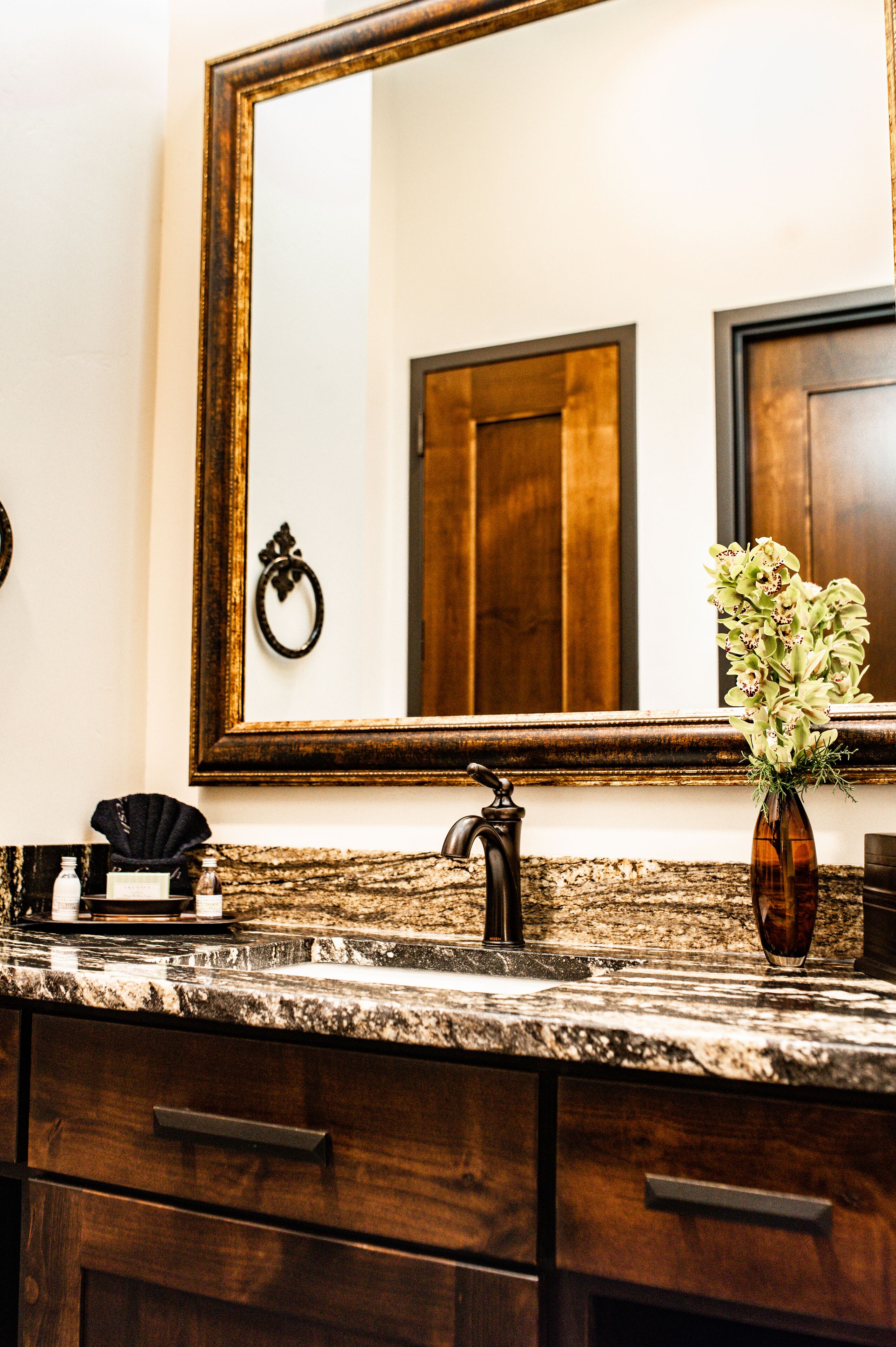A bathroom with a marble countertop, a large mirror, a vase with flowers, and a towel rack.
