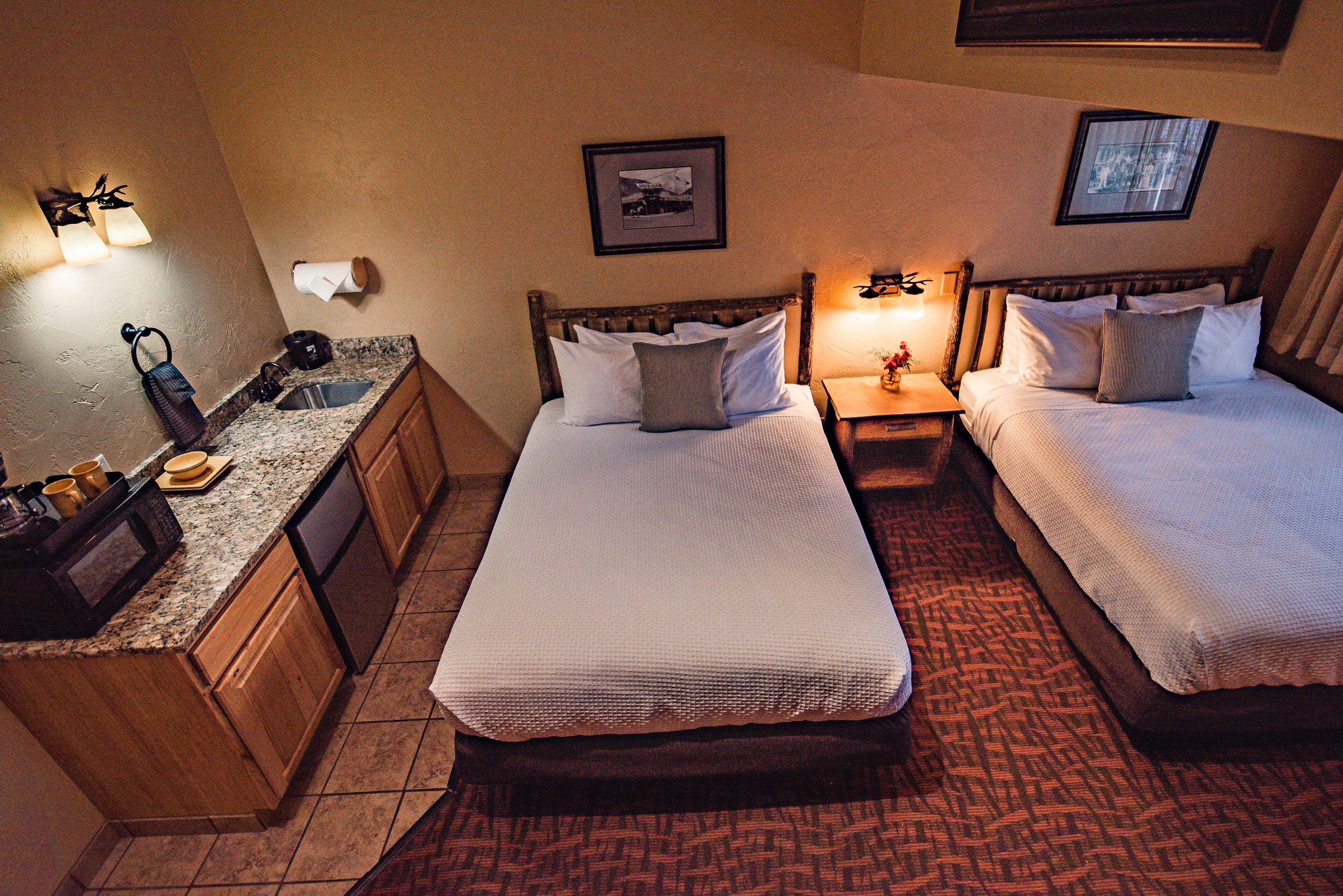 A hotel room with two beds, a small bathroom, and a kitchenette.