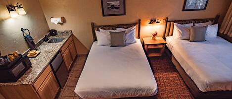 A hotel room with two beds, a small bathroom, and a kitchenette.