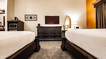 Ein Hotelzimmer mit zwei Betten, einem Flachbildfernseher, einem Schminktisch, einer Mikrowelle, einer Lampe und einem Spiegel.