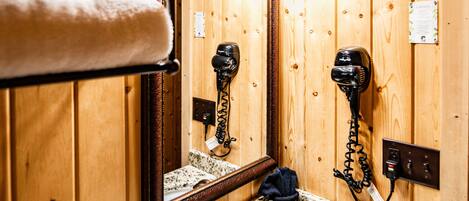 A wooden cabin-style bathroom with a granite countertop sink, a towel rack with towels, a hairdryer, and a mirror.