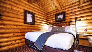 A log cabin bedroom with a bed, wooden walls, framed pictures, and a nightstand.