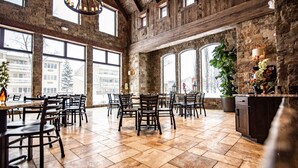 A spacious dining area with high ceilings and large windows, featuring a rustic stone wall and wooden beams. - Elk Country Inn (Jackson)