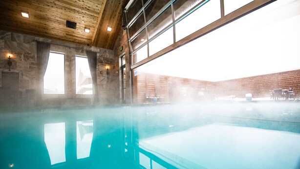 A large indoor swimming pool with clear water, wooden ceiling beams, and large windows allowing natural light. - Elk Country Inn (Jackson)