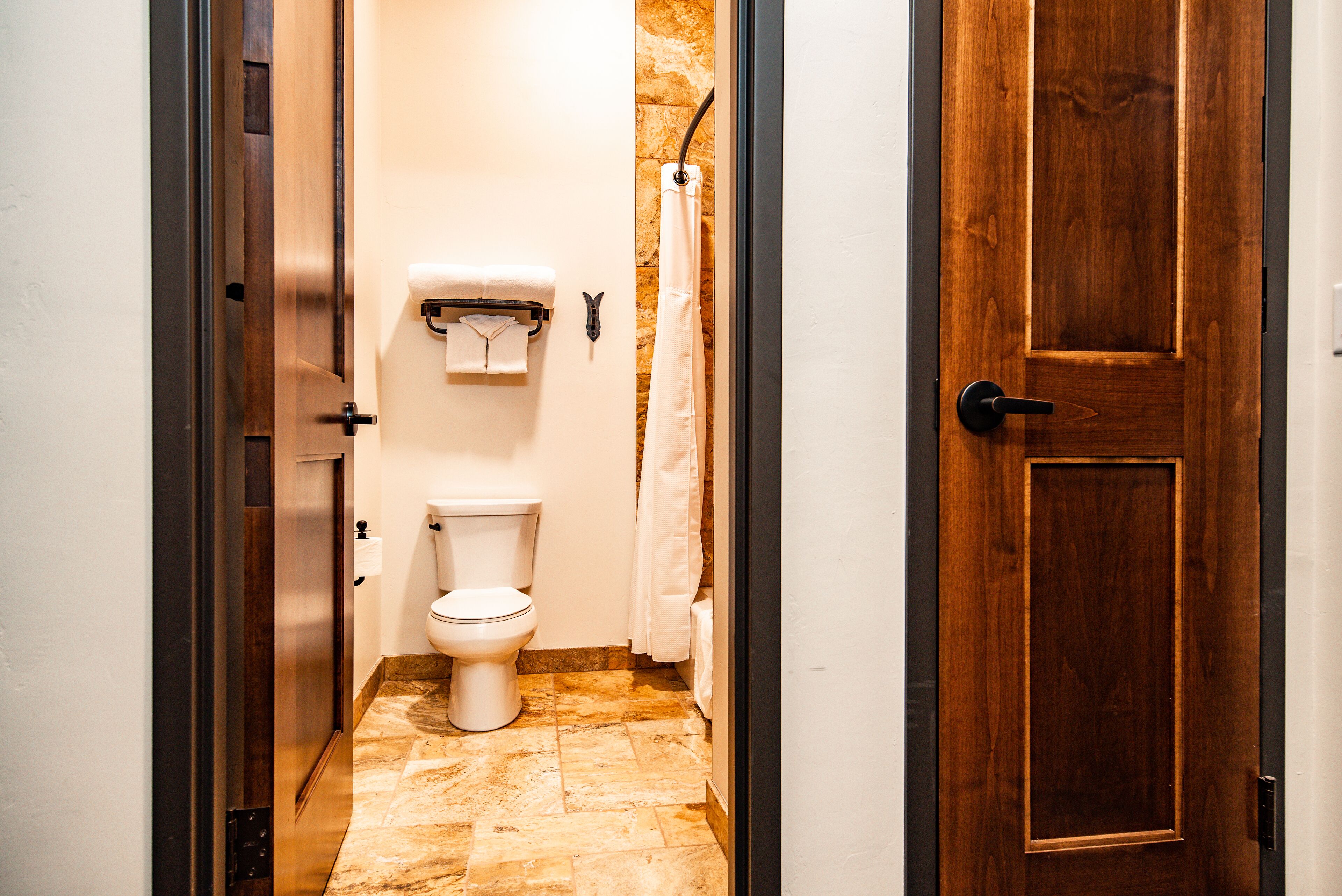A bathroom with a toilet, a shower curtain, and a wooden door.