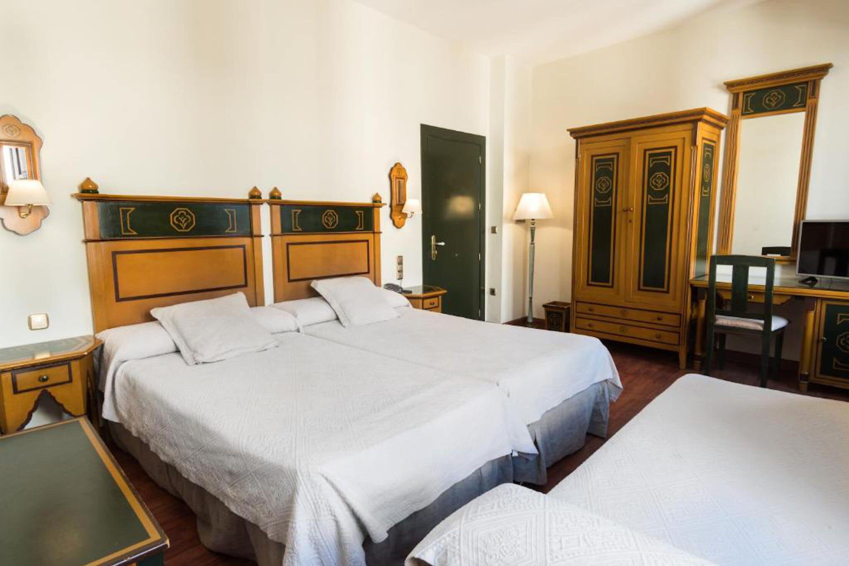 A hotel room with two beds, a desk, a chair, and a wardrobe.
