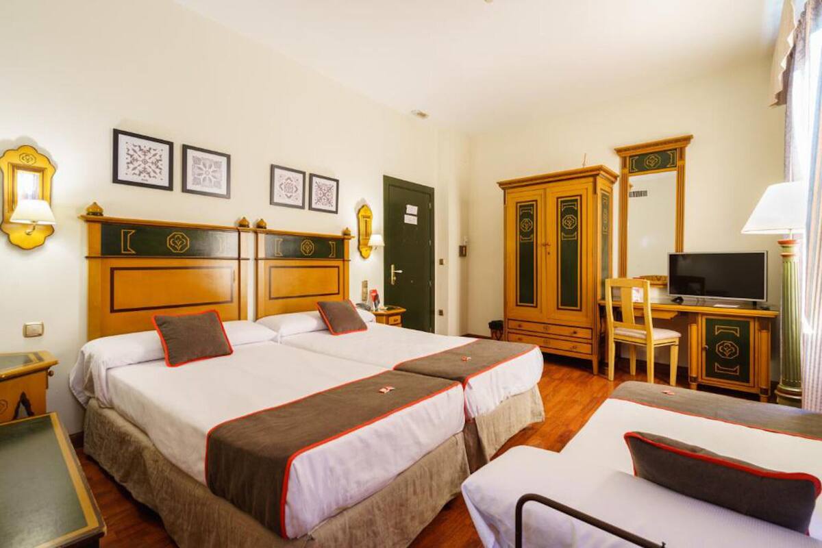 Quarto de hotel com duas camas, uma escrivaninha, televisão e guarda-roupa.