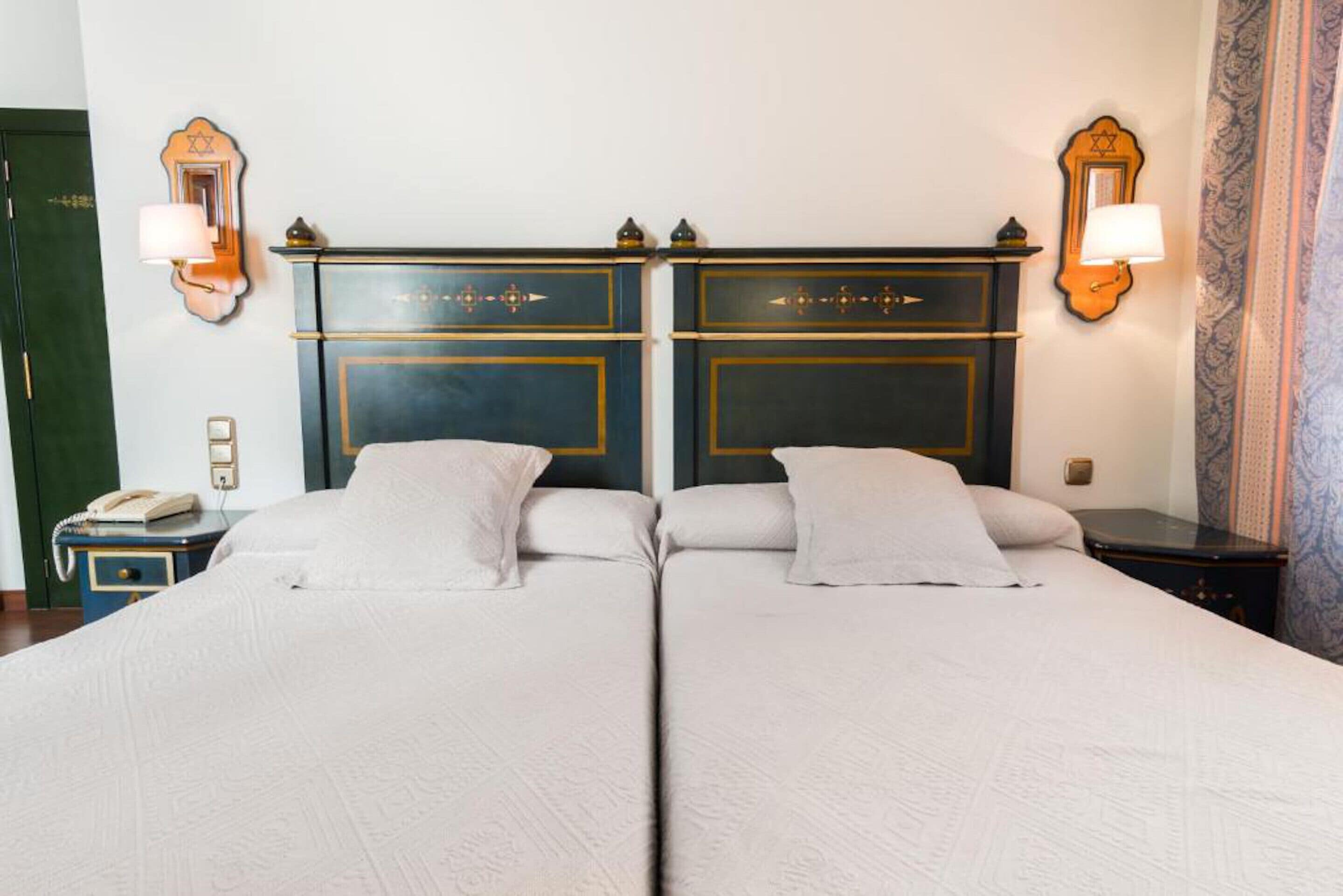 Una cama doble con cabecera, lámparas de noche y un teléfono en la mesita.