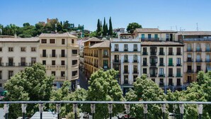 A row of multi-story buildings with balconies, a clear sky, and trees in the foreground.