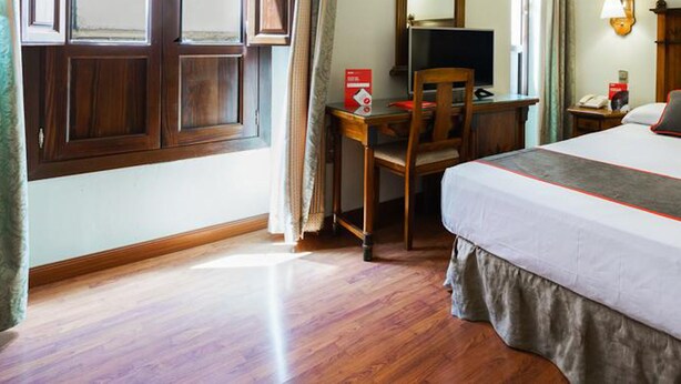 A hotel room with a bed, a desk, a chair, and a window.