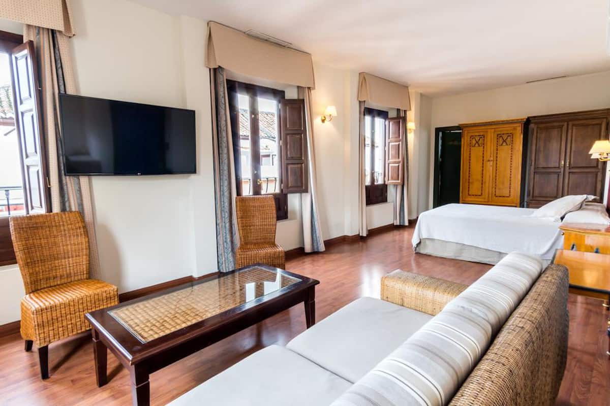 Quarto de hotel com uma cama grande, um sofá, uma televisão e um guarda-roupa de madeira.