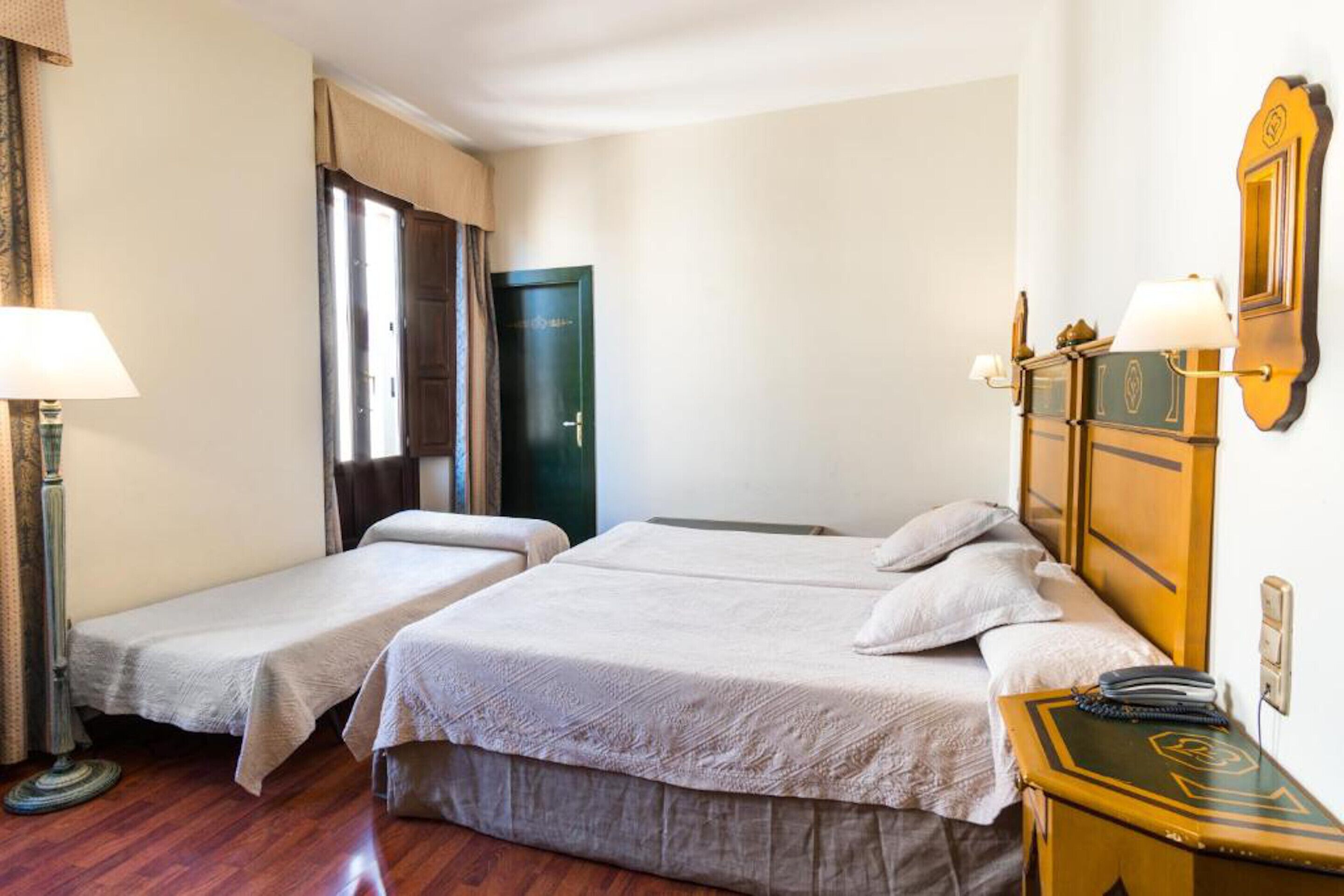 Una habitación de hotel con dos camas individuales, una mesita de noche de madera, una lámpara y una puerta.