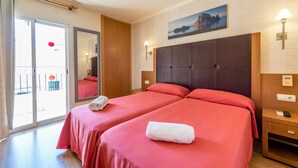 Habitación de hotel con dos camas, un ventanal grande, un ventilador de techo y un cuadro en la pared.