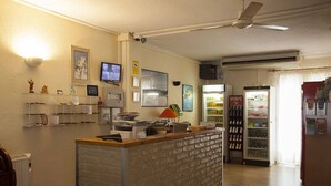 Una zona de recepción con mostrador de ladrillo, ventilador de techo, televisor y refrigerador lleno de bebidas.