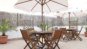 Un patio al aire libre con mesas y sillas redondas, rodeado de sombrillas, y una pared decorativa al fondo.