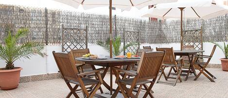 An outdoor patio with round tables and chairs, surrounded by umbrellas, and a decorative wall in the background.