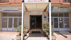 La entrada al Hostal Europa Púnico, con un acceso cubierto, plantas en macetas y carteles que indican biblioteca y librería.