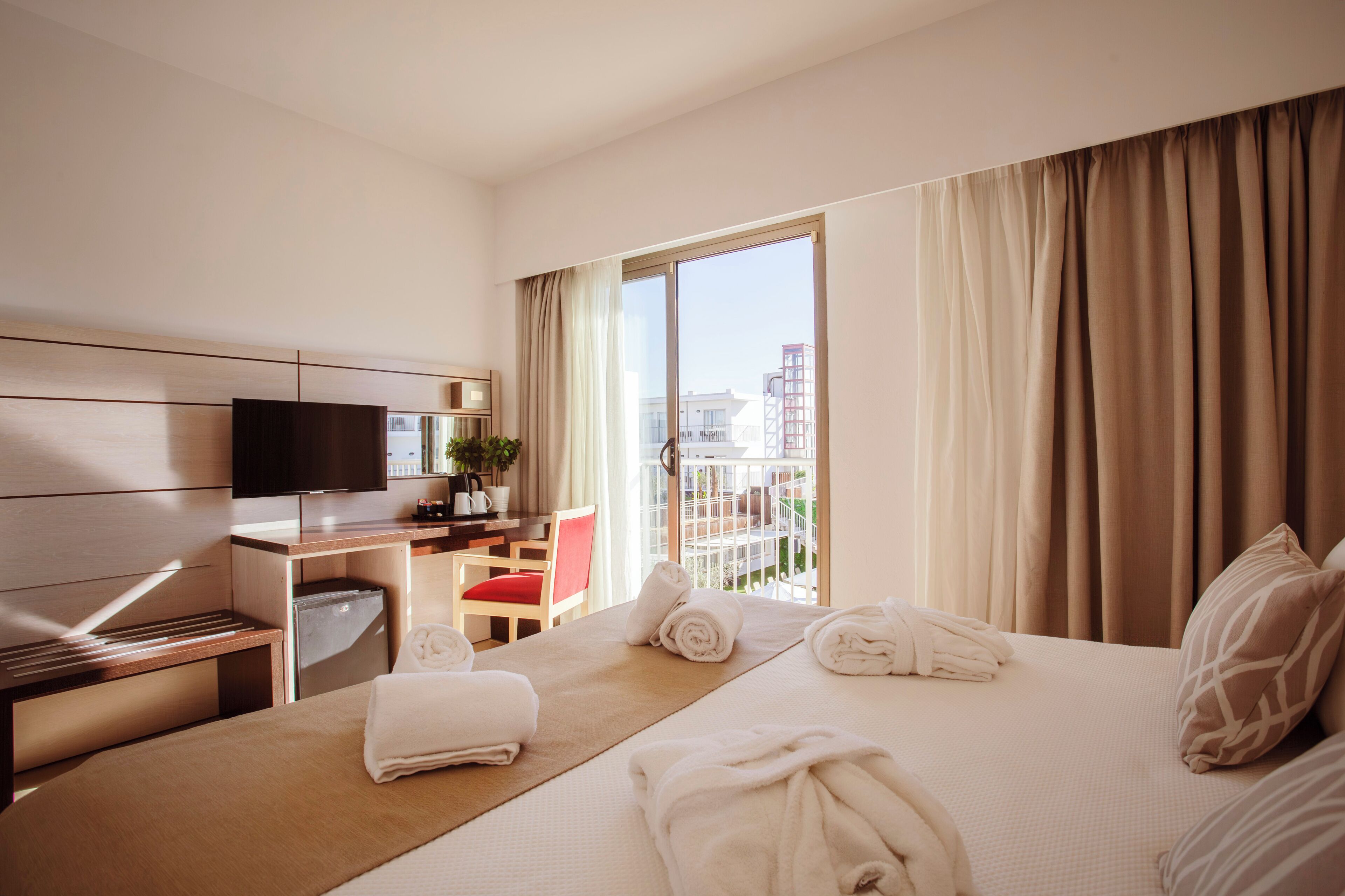 A hotel room with a bed, a desk, a television, a chair, and a window with curtains.