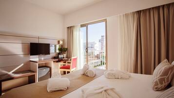 Habitación de hotel con cama, escritorio, televisor, silla y ventana con cortinas.
