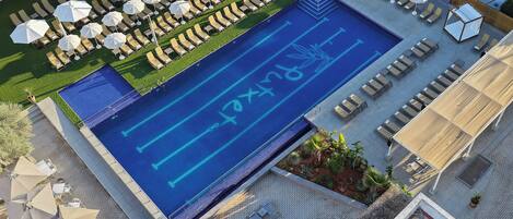 Eine Vogelperspektive auf ein Hotel-Pool-Gelände mit Liegestühlen, Sonnenschirmen und einem Pool mit blauen Markierungen.