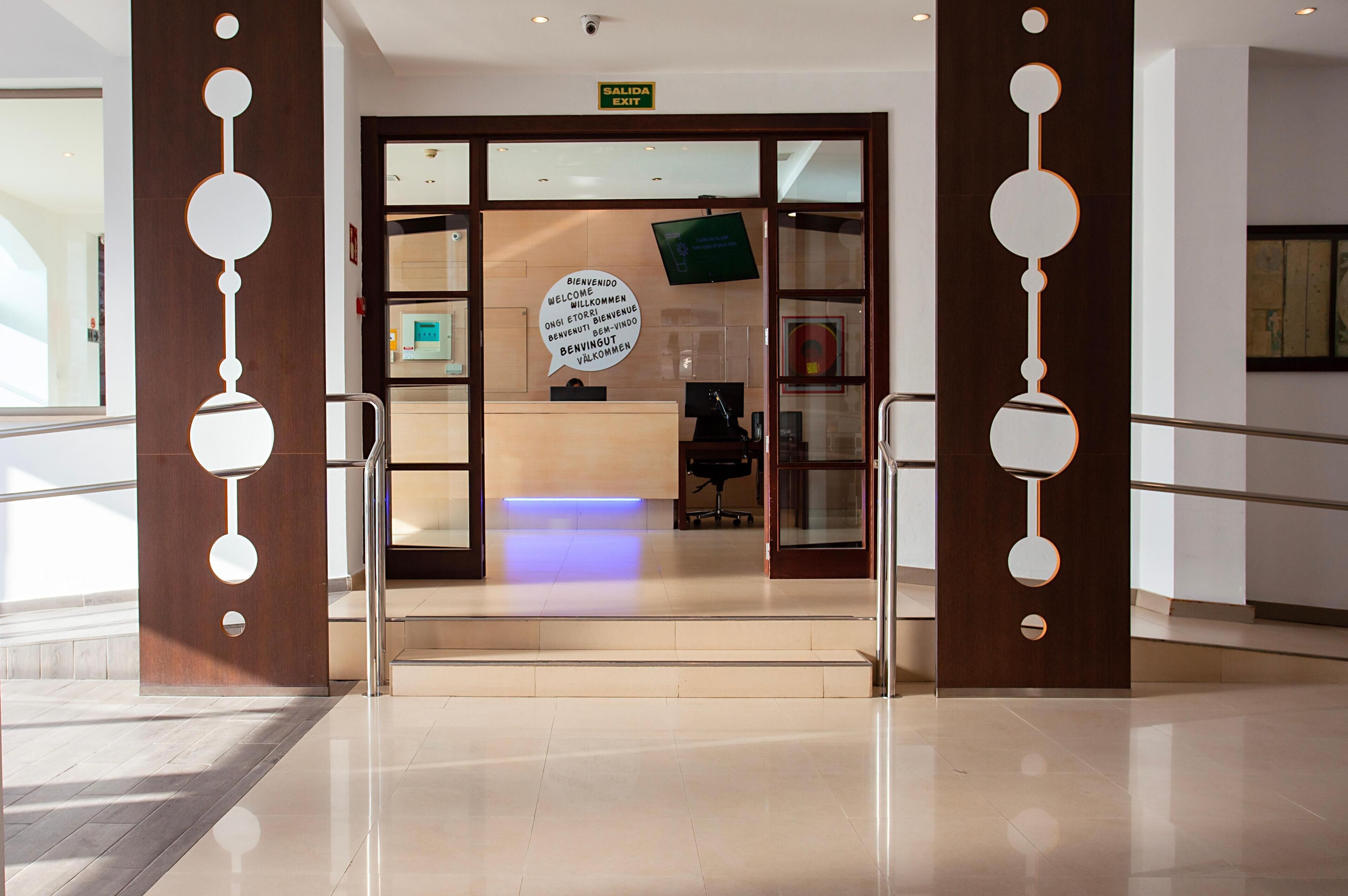 L’entrée d’un hôtel, avec un comptoir d’accueil, un écran numérique et un panneau indiquant la sortie.