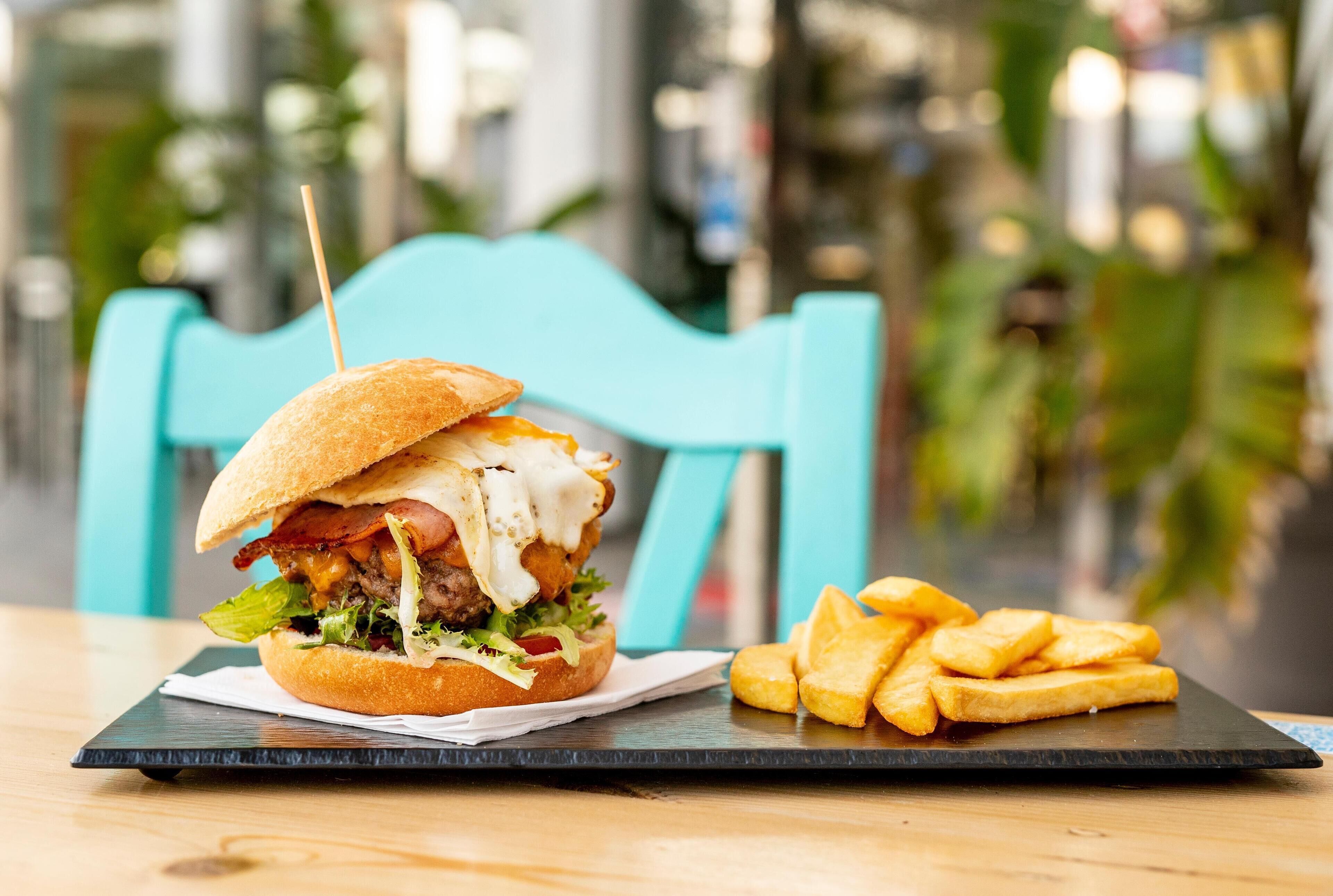Ein Burger mit Pommes auf einem schwarzen Teller auf einem Holztisch.