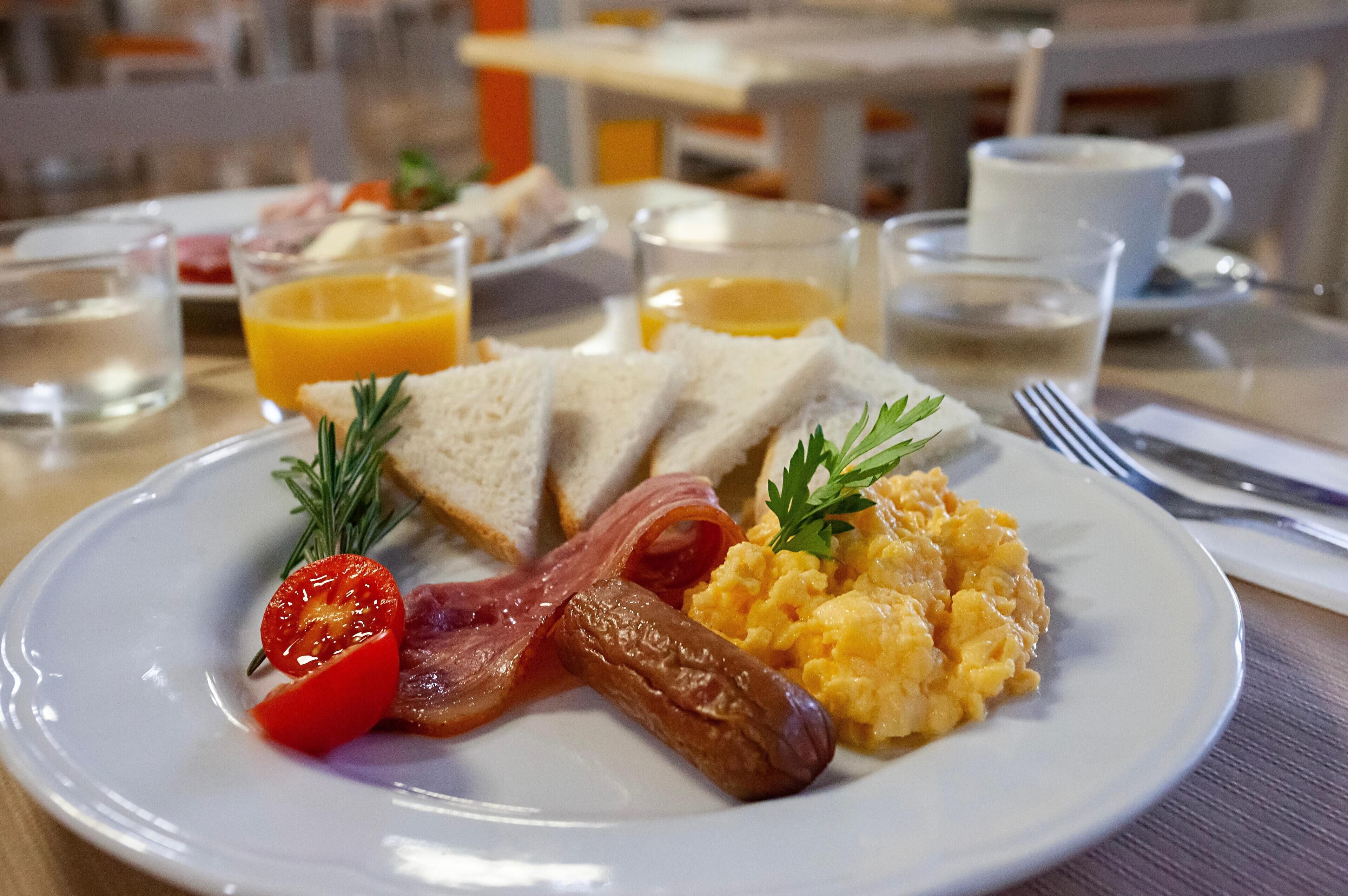Un plato de desayuno con tostadas, tocino, huevos revueltos y tomate.