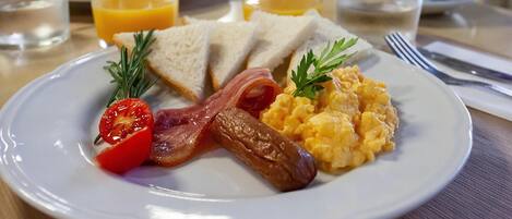 A breakfast plate with toast, bacon, scrambled eggs, and a tomato.