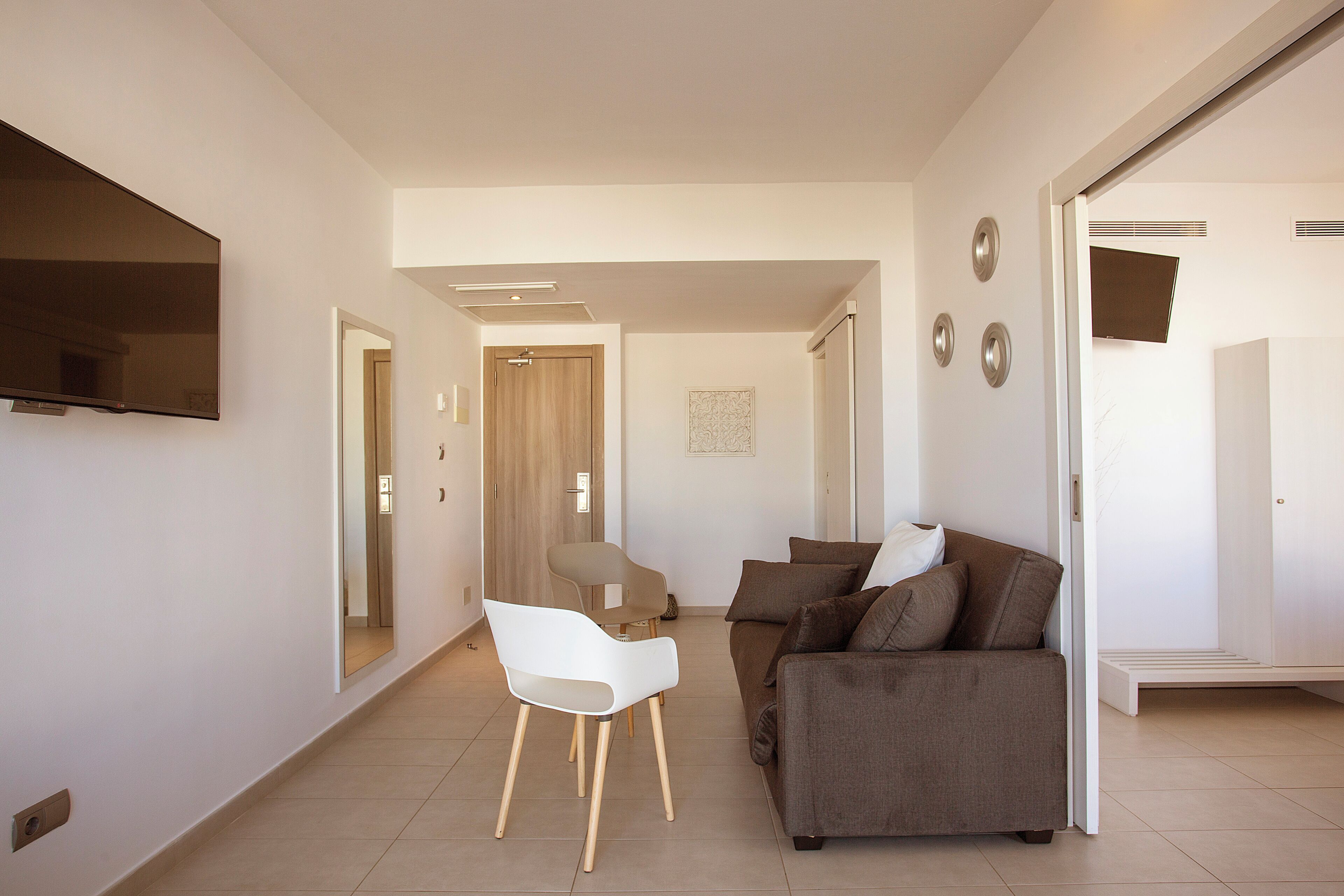 Een moderne woonkamer met een bank, een witte stoel en een flatscreen televisie aan de muur.