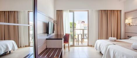 Habitación de hotel con dos camas, televisión, escritorio y vistas al exterior.