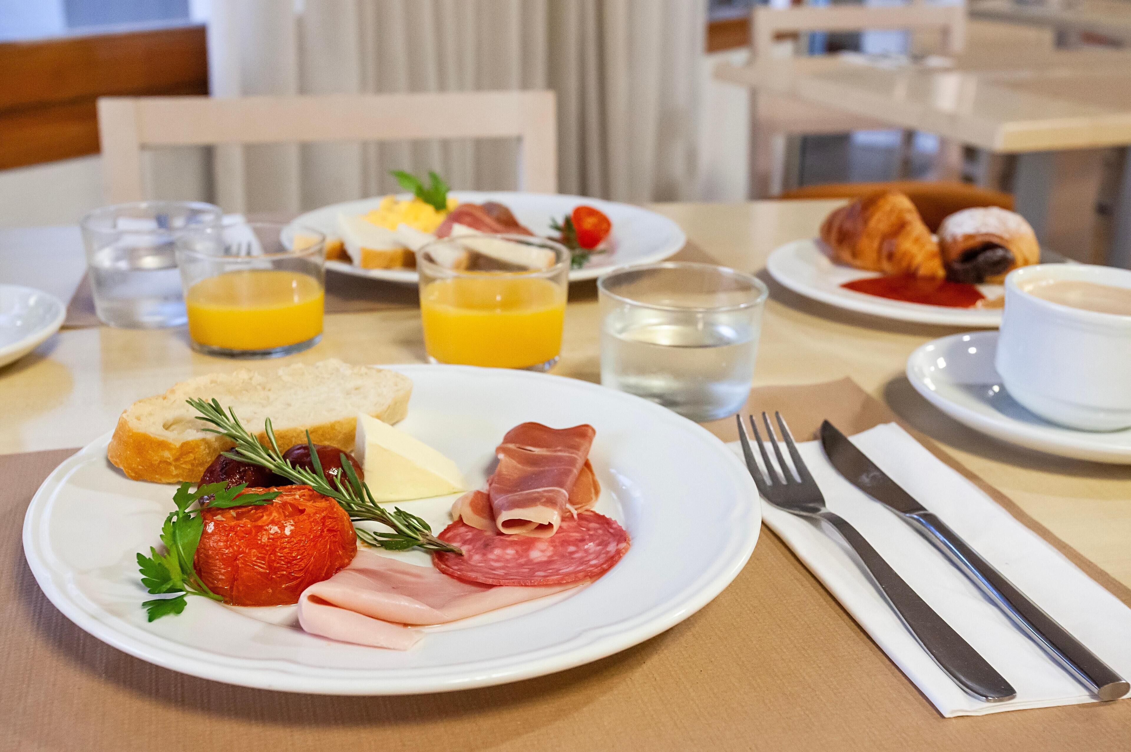 A breakfast setting with plates of food, glasses of orange juice, water, and a croissant.