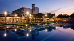 Zona de piscina hotelera con tumbonas y sombrillas, un edificio con torre y cielo despejado.