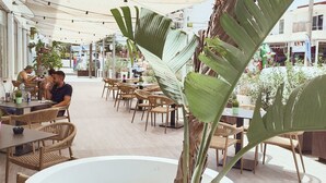Un café al aire libre con mobiliario de mimbre y plantas en macetas.