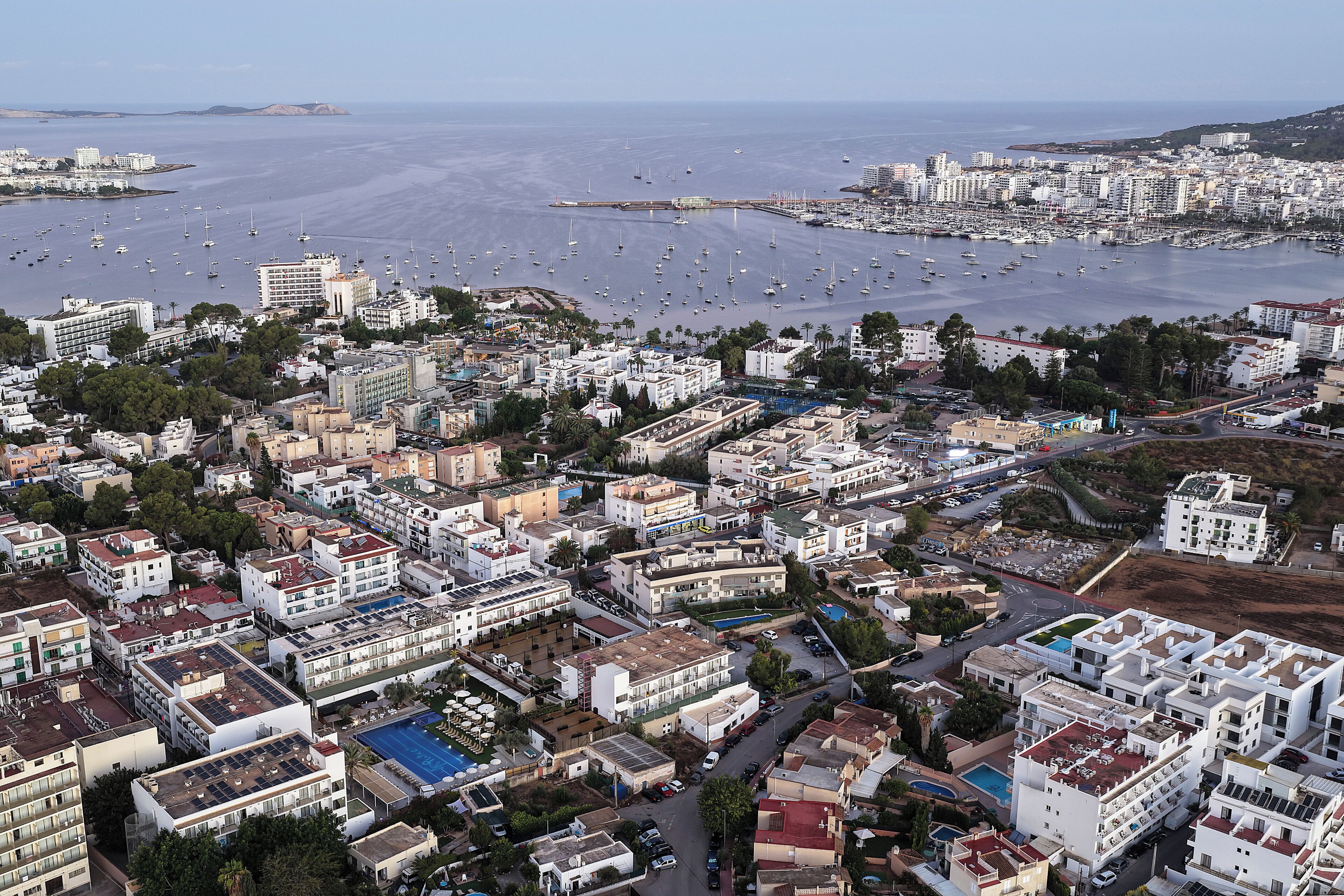 An aerial view of a coastal city with dense urban development, a marina with numerous boats, and a variety of building types including residential and commercial structures.