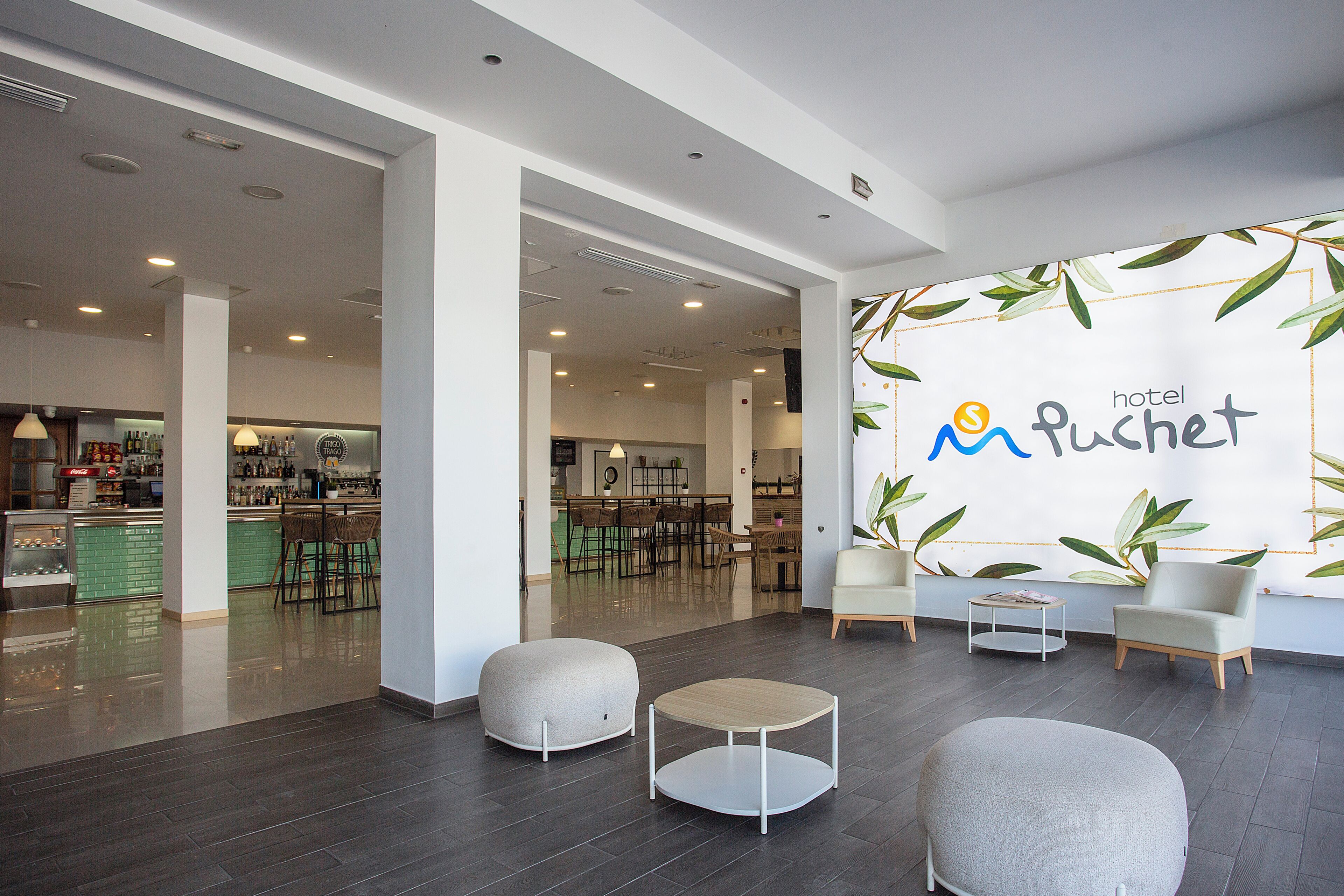 Un hall de hotel con zona de bar, asientos y una pared con el nombre del hotel.